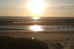 A beach with the sun low on the horizon, casting a reflection on the water. - Holiday apartment with 2 bedrooms (Wangerland)