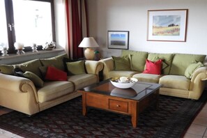 Ein Wohnzimmer mit zwei Sofas, einem Couchtisch und einer Lampe. An den Wänden befinden sich gerahmte Bilder.
