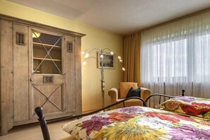 Een slaapkamer met een bed, een houten garderobe, een stoel en een vloerlamp.