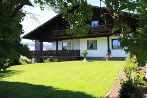 A two-story building with a balcony, a well-maintained lawn, and a flower bed. - 5-star country house Keller (Bischofsmais)