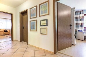 Ein Flur mit gerahmten Bildern an der Wand, einer Tür und einem Wohnbereich mit Sofa und Vorhängen.