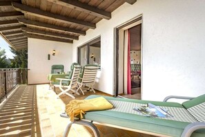 A covered outdoor seating area with a table and chairs, a lounge chair, and a sliding glass door leading to an interior space. - 5-star country house Keller (Bischofsmais)