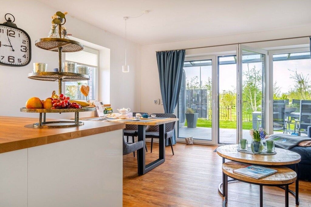 Ett modernt kök med en bänkskiva i trä, ett våningshögt fruktställ och en matplats med ett bord och stolar.