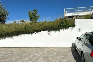 Ein Parkplatz mit einer weißen Wand und einem geparkten Auto rechts.