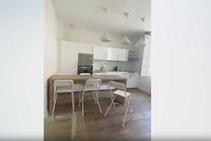 A modern kitchen with white cabinets, a central island, and a dining area with metal chairs. - Charming Apartment 1BR/4P - Le Marais (Paris)