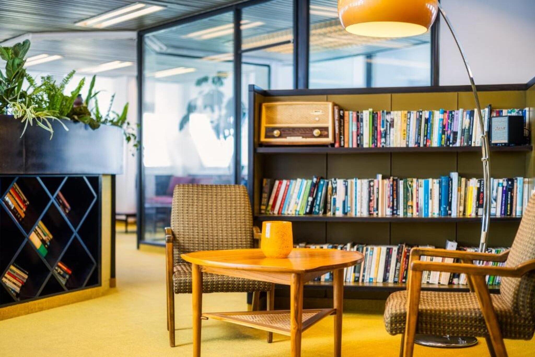 A modern reading area with a bookshelf, two chairs, a small table, and a lamp.