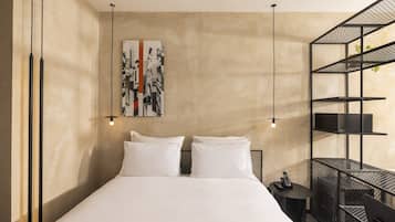 Quarto de hotel com uma cama, duas mesas de cabeceira, uma obra de arte na parede e uma estante de metal.