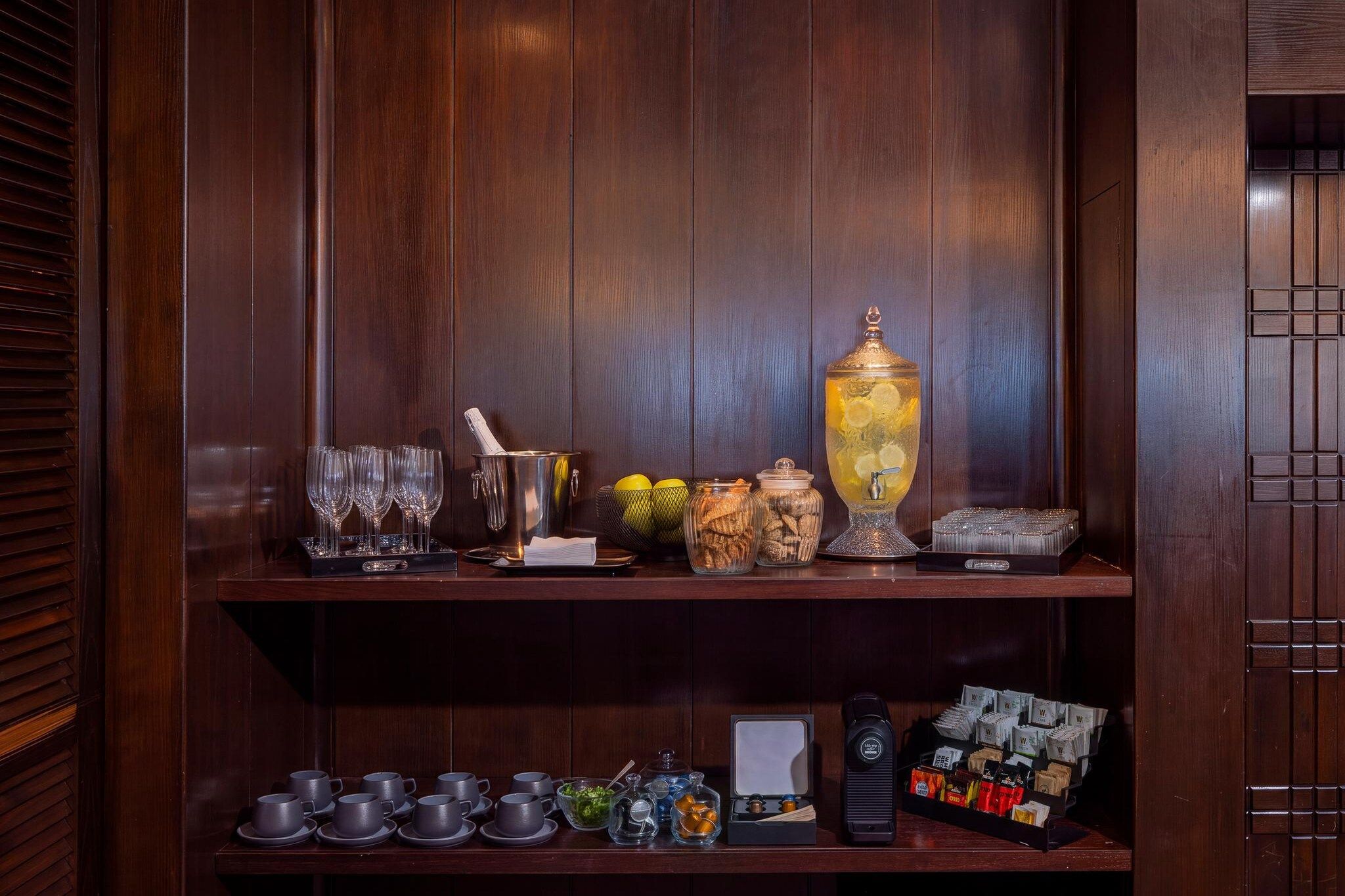 A wooden bar area with glasses, a cocktail shaker, a punch bowl, and various snacks.