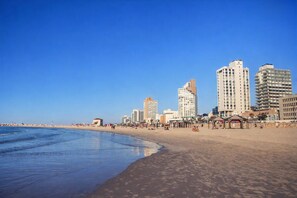 Ein Strand mit einer Stadtlandschaft im Hintergrund, darunter hohe Gebäude und ein klarer, blauer Himmel.
