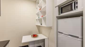 Een compacte kitchenette met een witte koelkast, een magnetron en een klein wit schapjesrek.