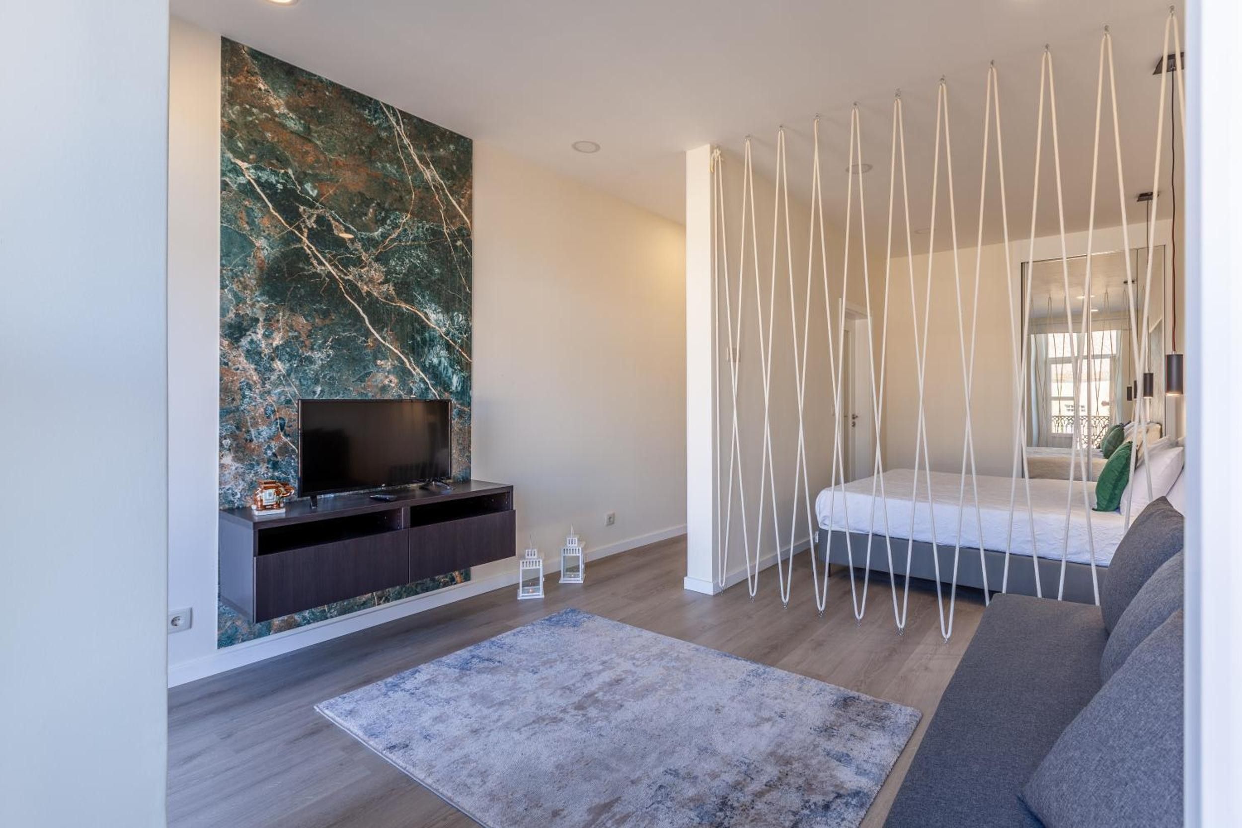 Een moderne woonkamer met een flatscreen televisie, een marmeren wand, een witte touw gordijn, een bank en een kamerkleed met dessin.
