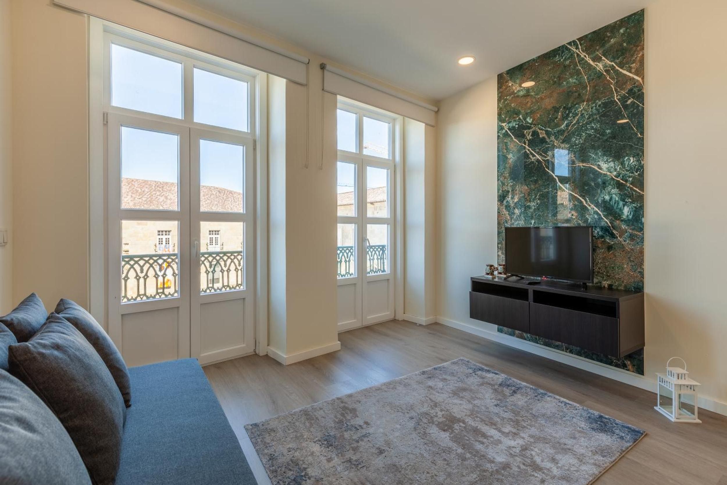 Een woonkamer met een bank, een flatscreen-televisie, een marmeren wand en grote ramen.