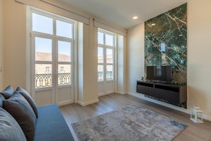 Ein Wohnzimmer mit einer Couch, einem Flachbildfernseher, einer Marmorwand und großen Fenstern.