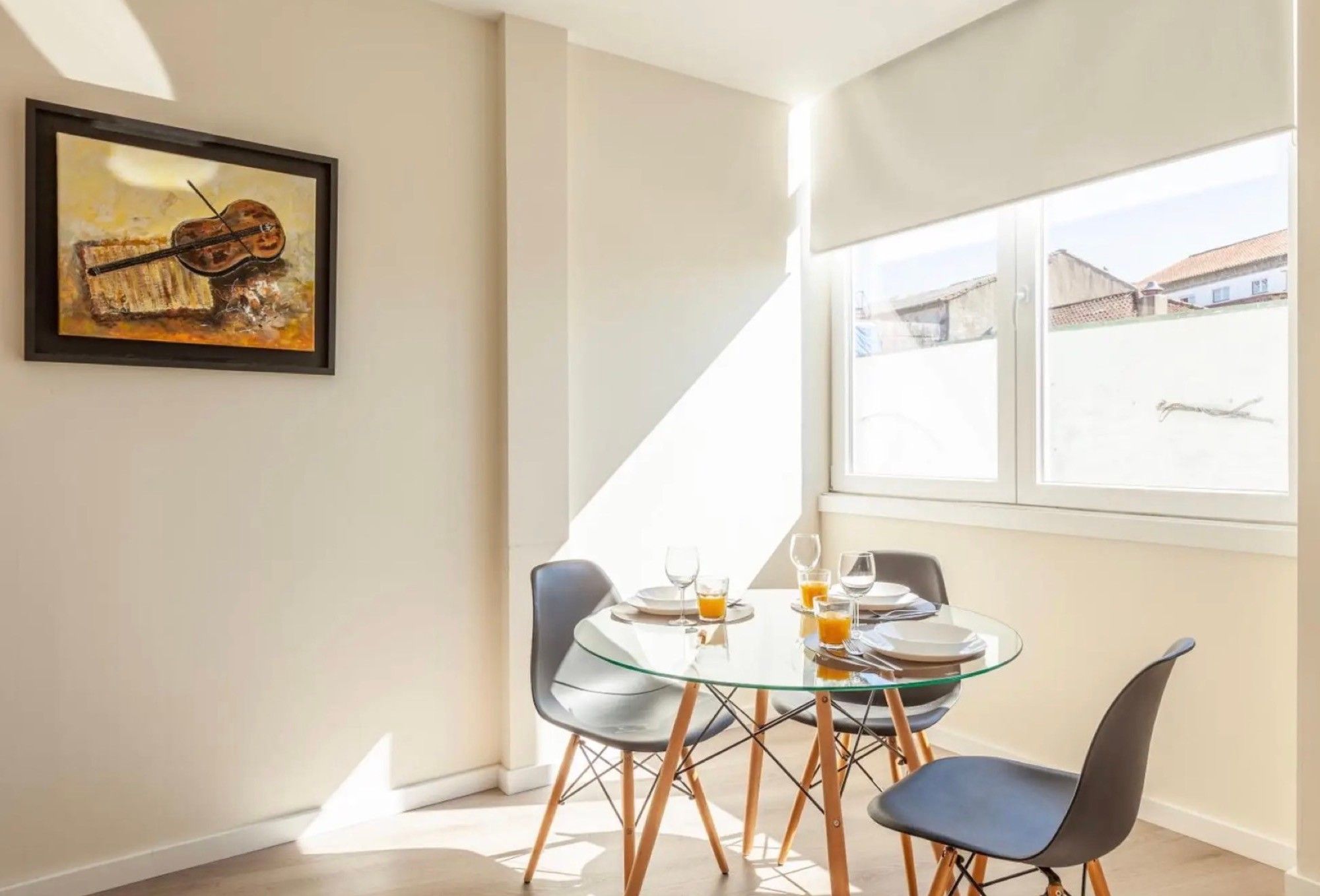 Een eetgedeelte met een glazen tafel, vier stoelen en een lijst met een schilderij aan de muur.