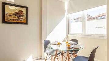 Een eetgedeelte met een glazen tafel, vier stoelen en een lijst met een schilderij aan de muur.