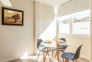 Ein Essbereich mit einem Glastisch, vier Stühlen und einem gerahmten Gemälde an der Wand.