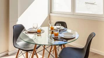 A modern dining area with a glass table and black chairs, featuring a breakfast setting with plates, glasses, and orange juice.