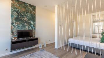 Un dormitorio moderno con una televisión sobre un mueble de madera oscura, una pared de mármol grande, una cama blanca con dosel y una alfombra gris.