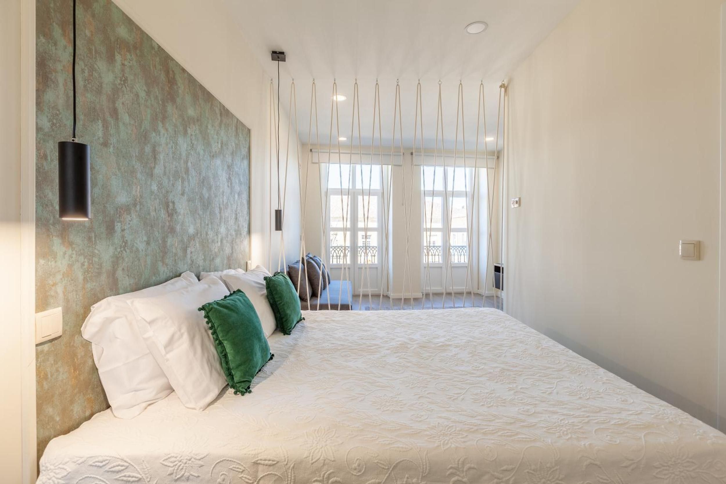Une chambre spacieuse avec un grand lit, un luminaire suspendu et une vue sur l’extérieur par les fenêtres.