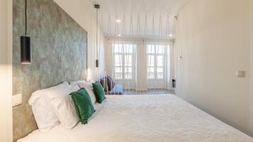 Une chambre spacieuse avec un grand lit, un luminaire suspendu et une vue sur l’extérieur par les fenêtres.