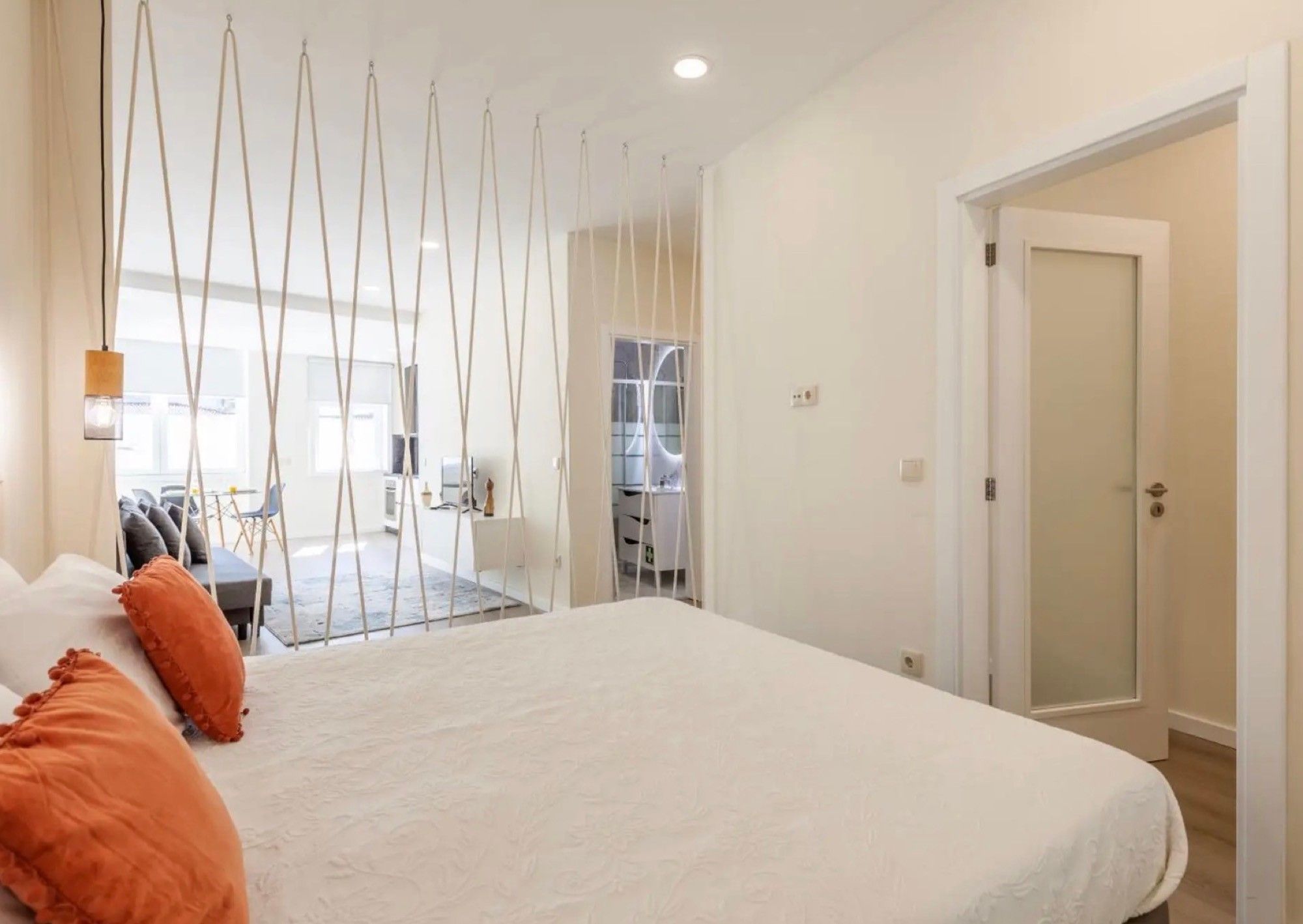 A bedroom with a large bed, a desk, and a chair. There is a door leading to another room.