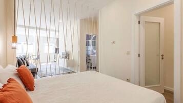 A bedroom with a large bed, a desk, and a chair. There is a door leading to another room.