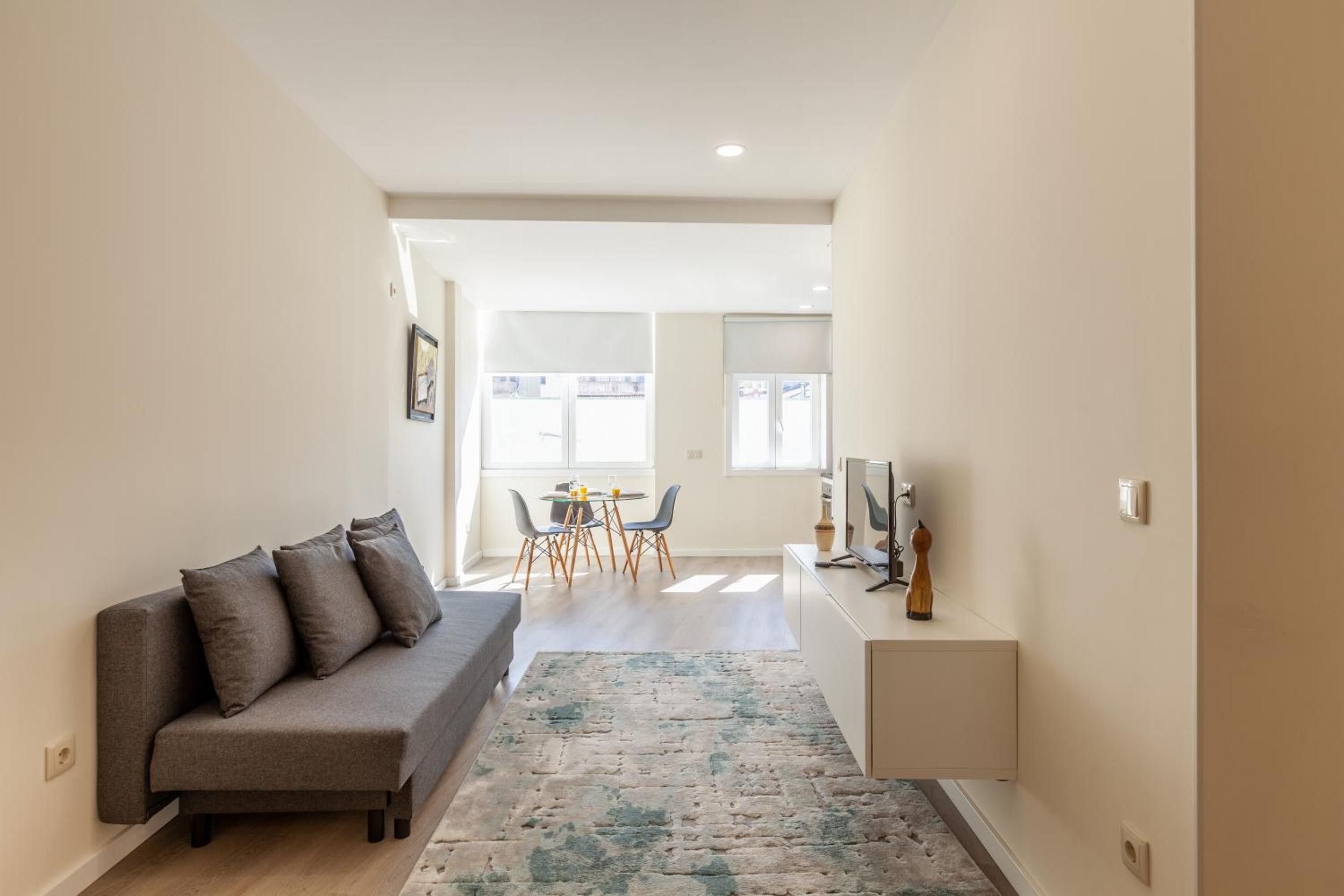 Una sala de estar moderna con un sofá gris, un comedor con una mesa y sillas, y un escritorio pequeño con una computadora.