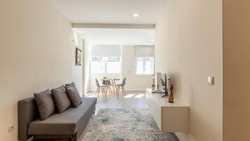 Una sala de estar moderna con un sofá gris, un comedor con una mesa y sillas, y un escritorio pequeño con una computadora.