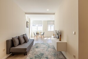 Ein modernes Wohnzimmer mit einem grauen Sofa, einem Essbereich mit Tisch und Stühlen und einem kleinen Schreibtisch mit einem Computer.