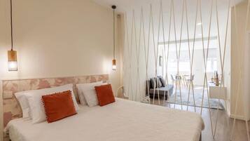 A bedroom with a large bed, a hanging light fixture, and a view of the living area.