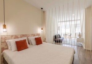Ein Schlafzimmer mit einem großen Bett, einer Hängeleuchte und Blick auf den Wohnbereich.