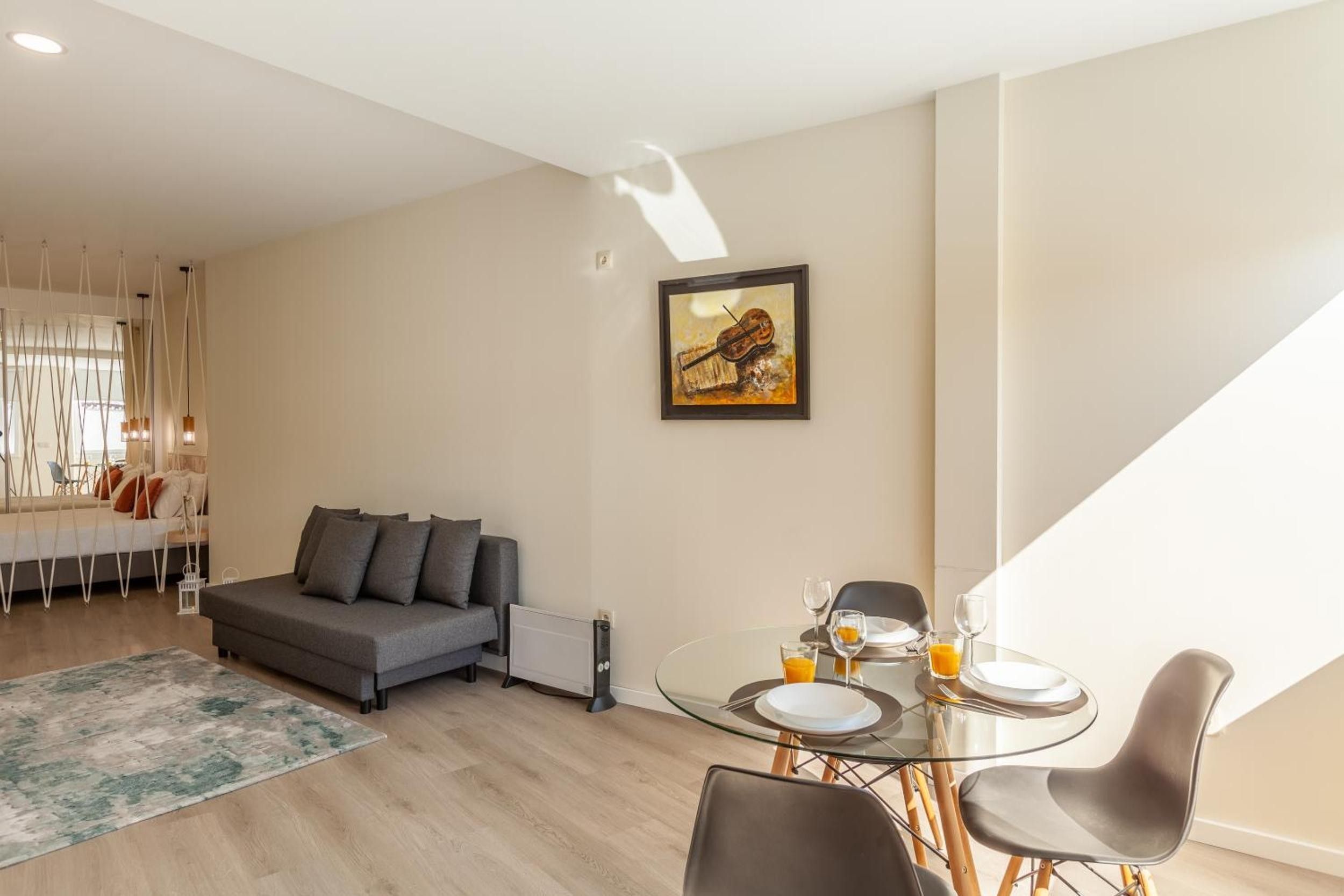 A modern living room with a sofa, a dining table with chairs, and a painting on the wall.
