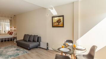 A modern living room with a sofa, a dining table with chairs, and a painting on the wall.