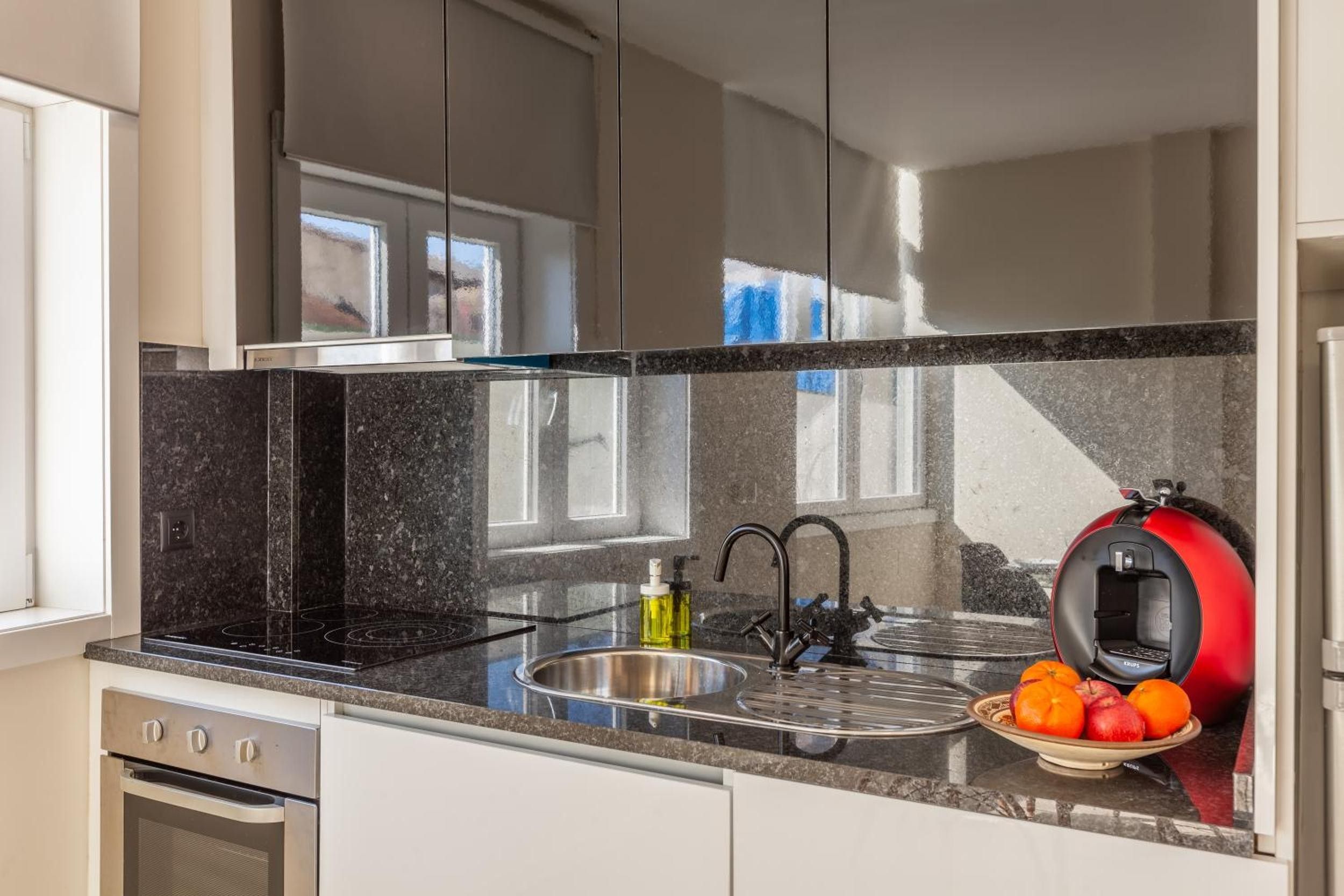 A modern kitchen with a black granite countertop, stainless steel sink, and a red coffee machine.