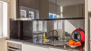 A modern kitchen with a black granite countertop, stainless steel sink, and a red coffee machine.