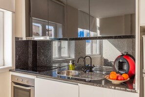 Una cocina moderna con encimera de granito negro, pileta de acero inoxidable y una cafetera roja.