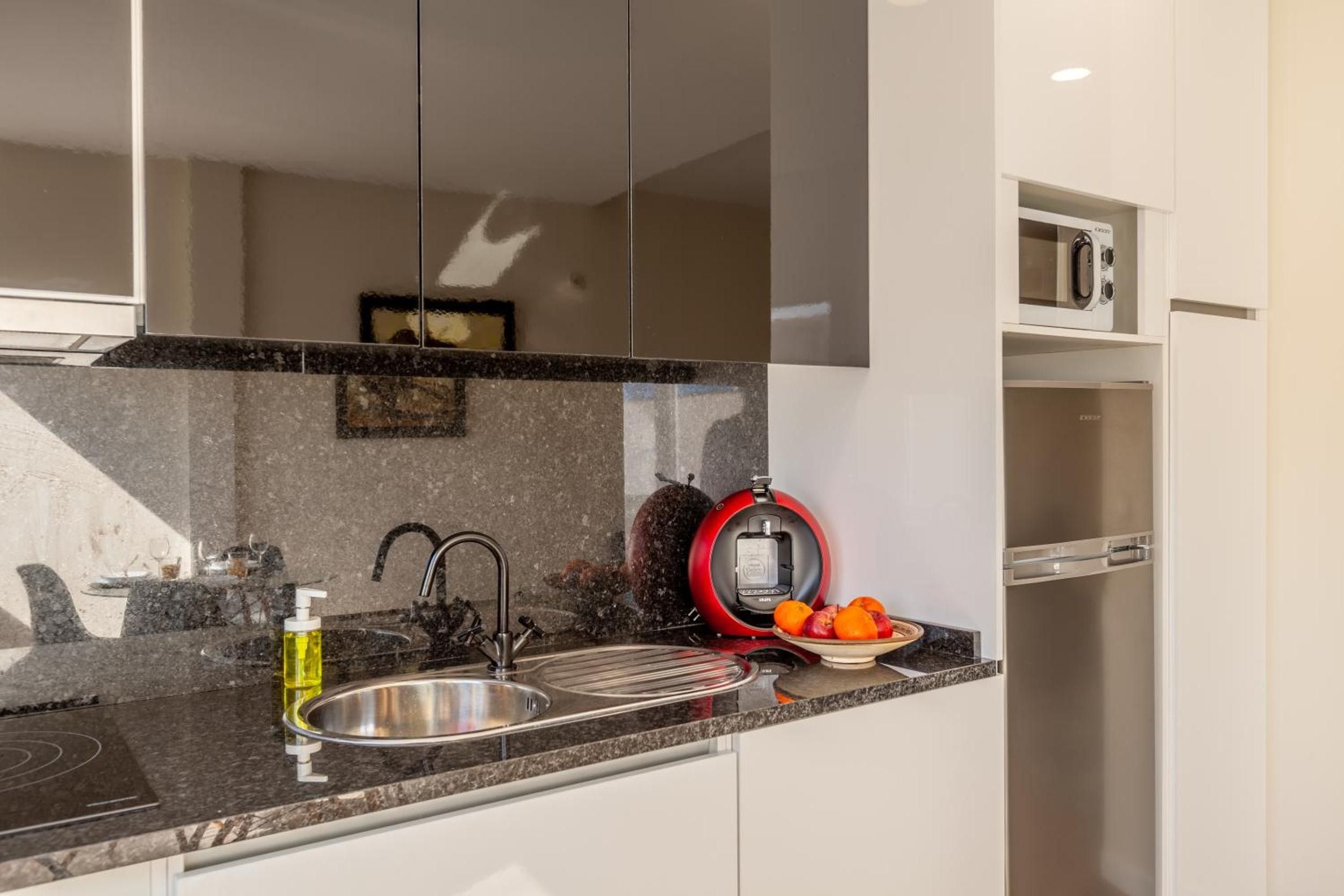 Una cocina moderna con un lavamanos de acero inoxidable, un hervidor rojo y un microondas.