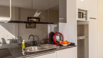 Una cocina moderna con un lavamanos de acero inoxidable, un hervidor rojo y un microondas.