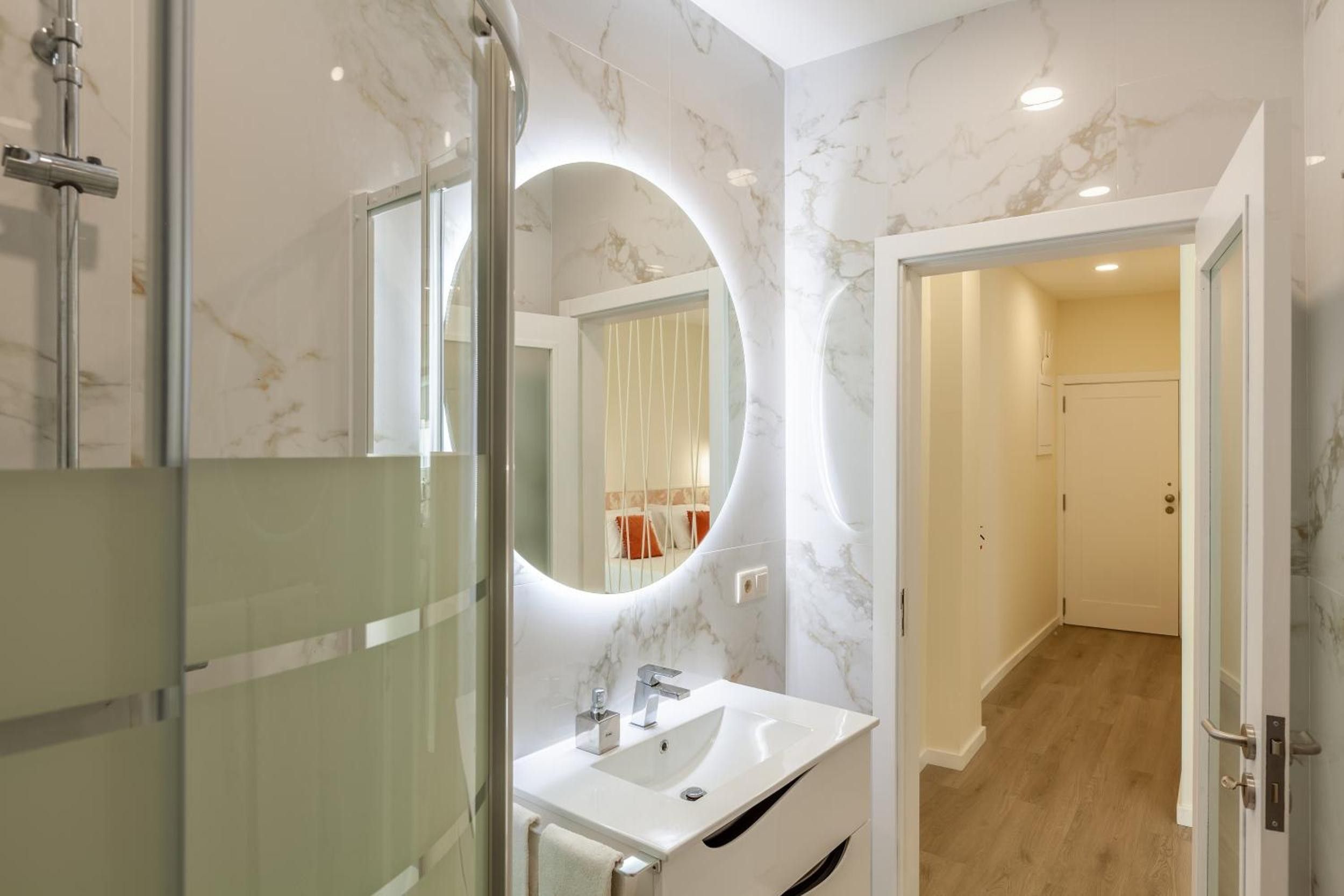 Un baño moderno con cabina de ducha de vidrio, un lavamanos blanco y pared con diseño de mármol.