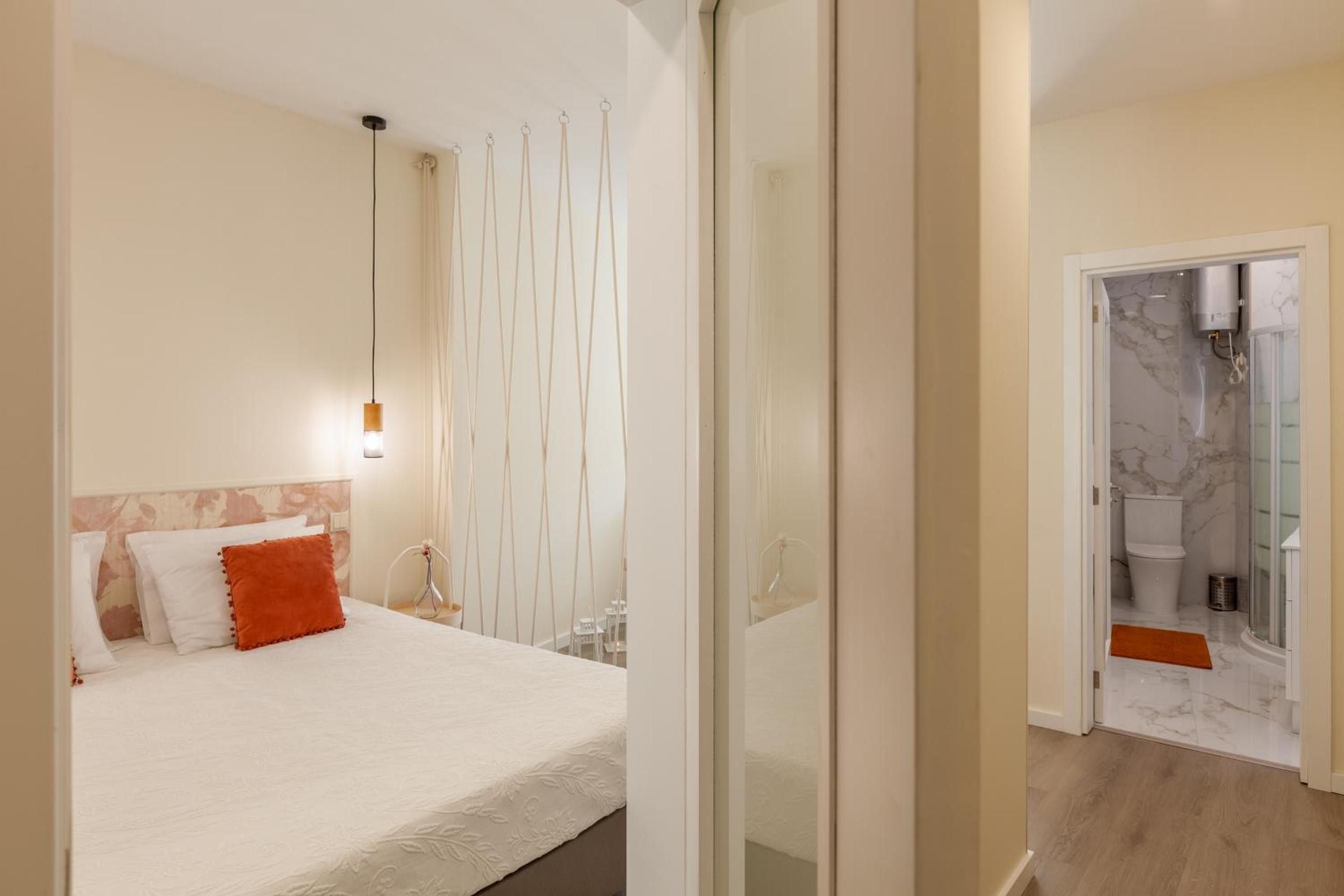 Une chambre d’hôtel avec un lit, un luminaire suspendu, une salle de bain avec douche et un sol en marbre.