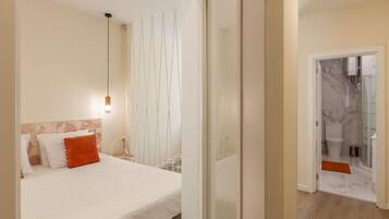 Une chambre d’hôtel avec un lit, un luminaire suspendu, une salle de bain avec douche et un sol en marbre.