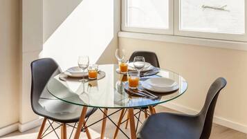 A modern dining area with a glass table and black chairs, featuring a breakfast setting with plates, glasses, and orange juice.