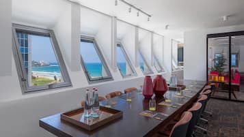 Un salón de conferencias con una mesa larga, múltiples sillas y vistas al océano a través de tragaluces.