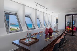 Un salón de conferencias con una mesa larga, múltiples sillas y vistas al océano a través de tragaluces.