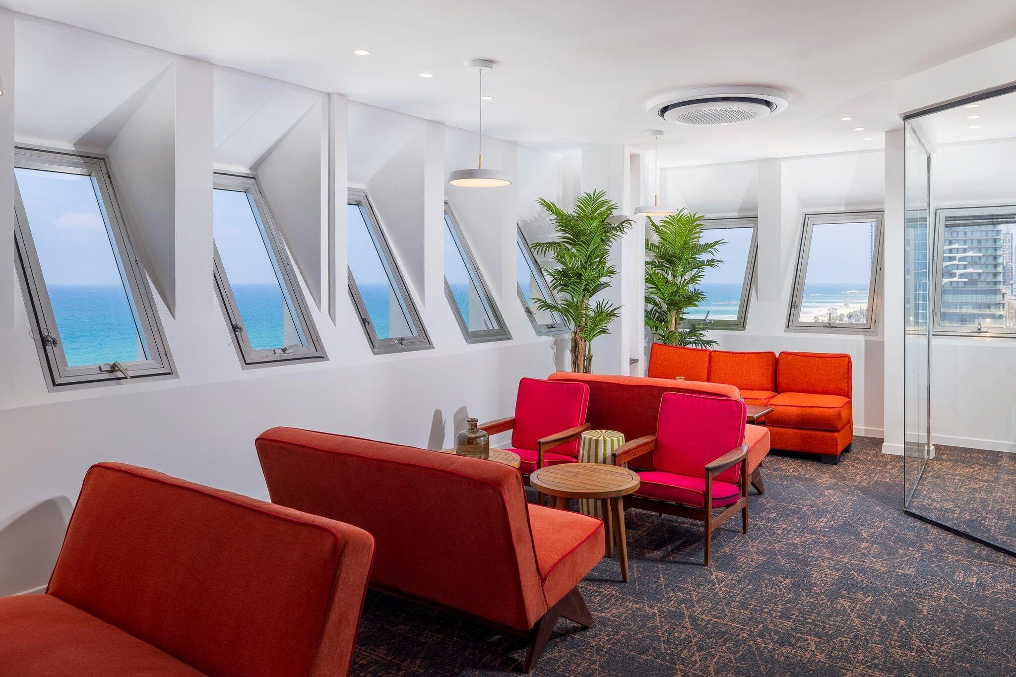Un salon moderne doté de plusieurs espaces de détente, de grandes fenêtres offrant une vue sur l’océan et d’un plafond pourvu d’un éclairage encastré.