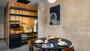 Un moderno comedor con una mesa redonda dispuesta para cuatro personas, rodeada de sillas de madera. Se observa una estantería negra con una obra de arte geométrica en la pared.