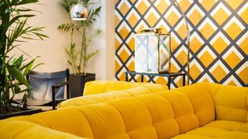 A yellow sofa in a room with a geometric patterned wall, a potted plant, and a small table with a lamp.