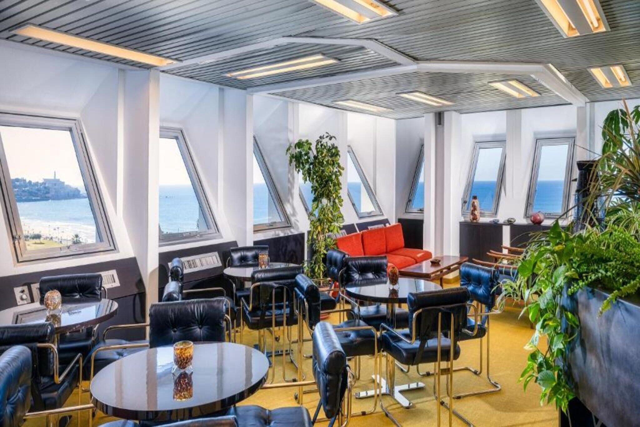 A modern interior with a high ceiling, multiple windows, and a seating area with tables and chairs.