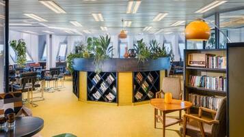 Eine moderne Bibliothek mit Bücherregalen, einer zentralen Sitzgruppe und großen Fenstern.