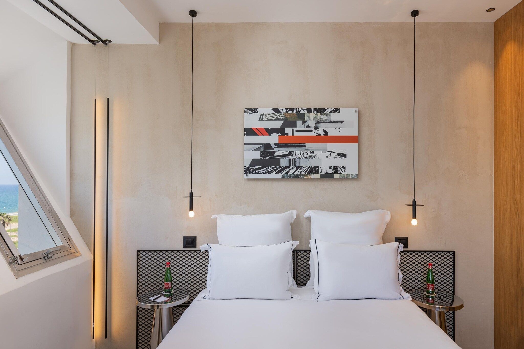 A modern bedroom with a large bed, two nightstands, a wall-mounted abstract art piece, and a window with a view.